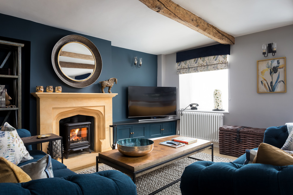Idée de décoration pour un grand salon champêtre fermé avec une salle de réception, un mur bleu, un poêle à bois, un manteau de cheminée en pierre, un téléviseur indépendant et un sol marron.