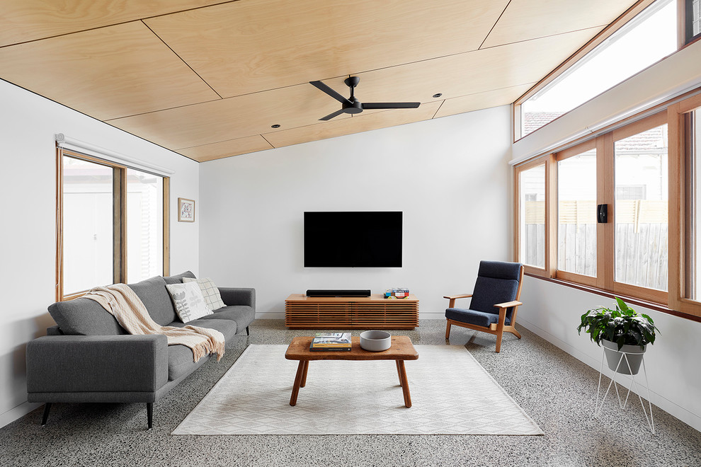 Стильный дизайн: открытая гостиная комната в современном стиле с белыми стенами, отдельно стоящим телевизором и серым полом - последний тренд