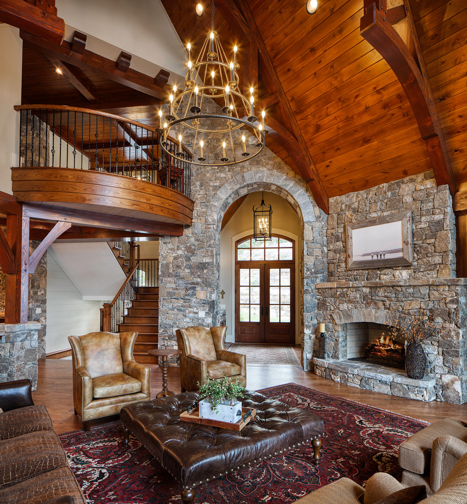 This is an example of a rustic living room in Other with grey walls, medium hardwood flooring, a standard fireplace, a stone fireplace surround and brown floors.