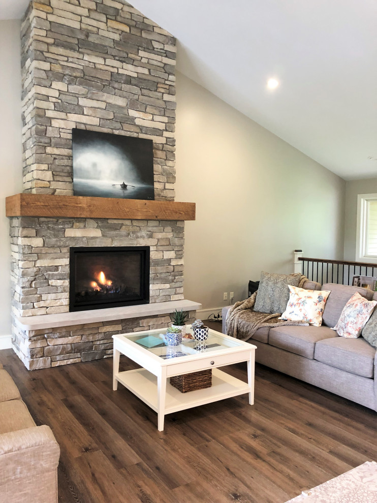 Cette image montre un grand salon traditionnel ouvert avec un mur gris, un sol en vinyl, une cheminée standard, un manteau de cheminée en pierre et un sol marron.