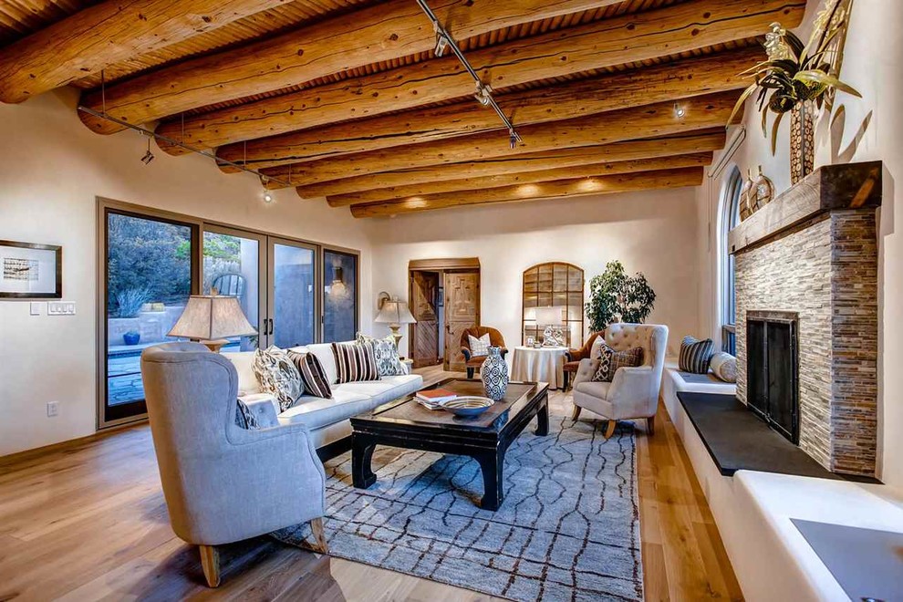 Living room - southwestern enclosed medium tone wood floor living room idea in Albuquerque with a stone fireplace, beige walls and a standard fireplace