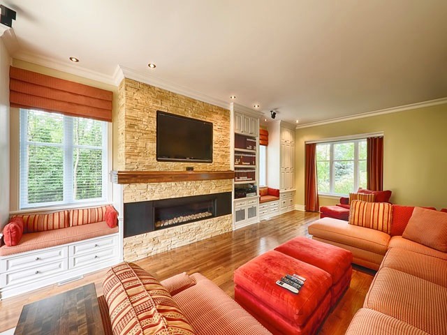 Cette image montre un grand salon traditionnel ouvert avec une salle de réception, un mur jaune, un sol en bois brun, une cheminée ribbon, un manteau de cheminée en pierre et un téléviseur encastré.
