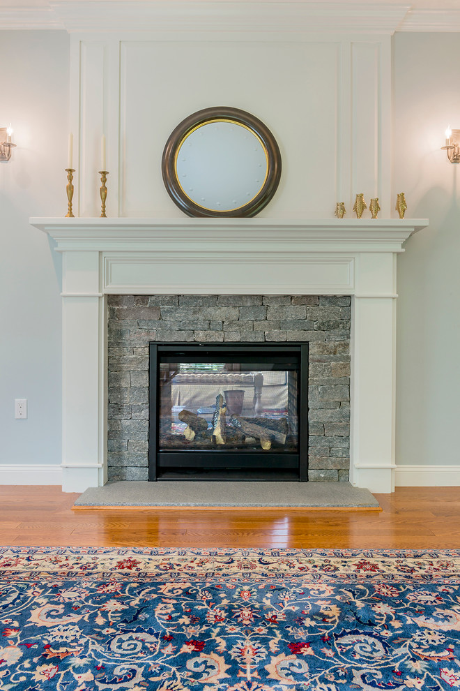 Imagen de salón para visitas abierto clásico renovado grande con paredes grises, suelo de madera en tonos medios, chimenea de doble cara y marco de chimenea de piedra
