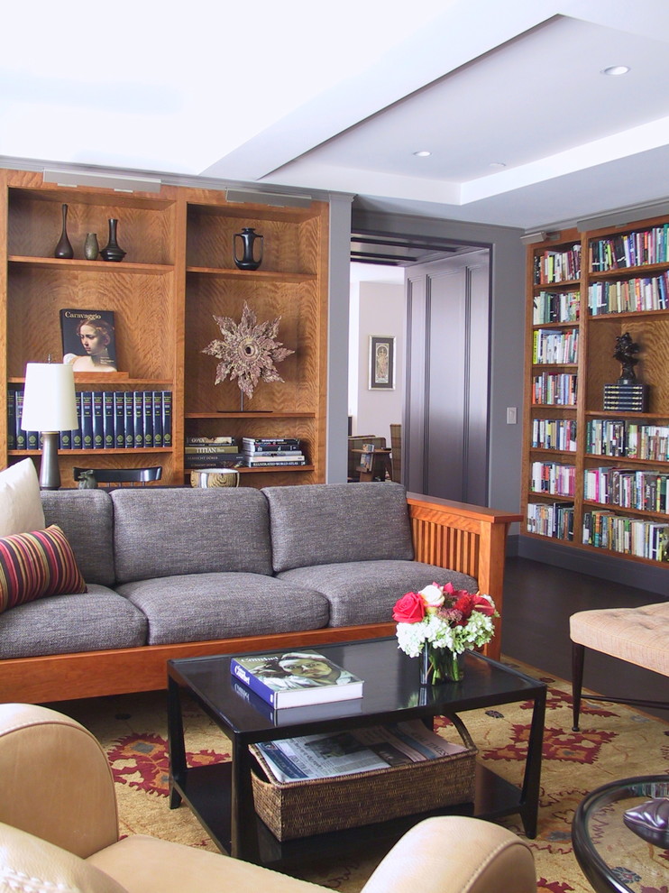 Cette photo montre un grand salon chic ouvert avec une bibliothèque ou un coin lecture, un mur gris, parquet foncé, aucune cheminée et un sol marron.
