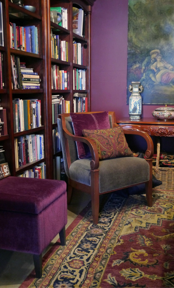 Cette image montre un salon bohème fermé avec un mur violet, sol en béton ciré, un manteau de cheminée en pierre et une bibliothèque ou un coin lecture.