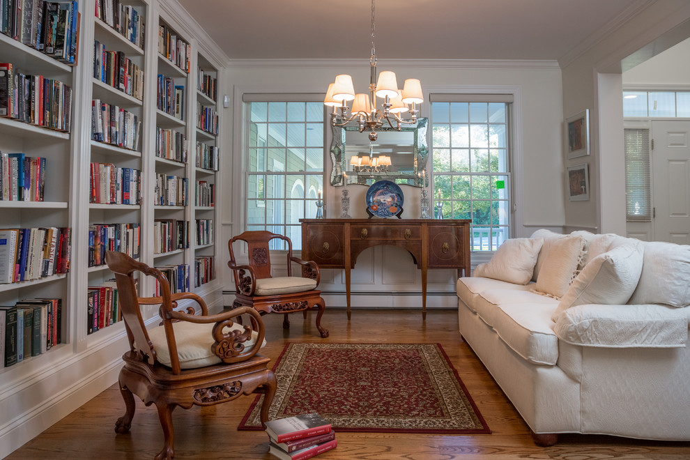 Ejemplo de biblioteca en casa abierta clásica sin televisor con paredes blancas y suelo de madera en tonos medios