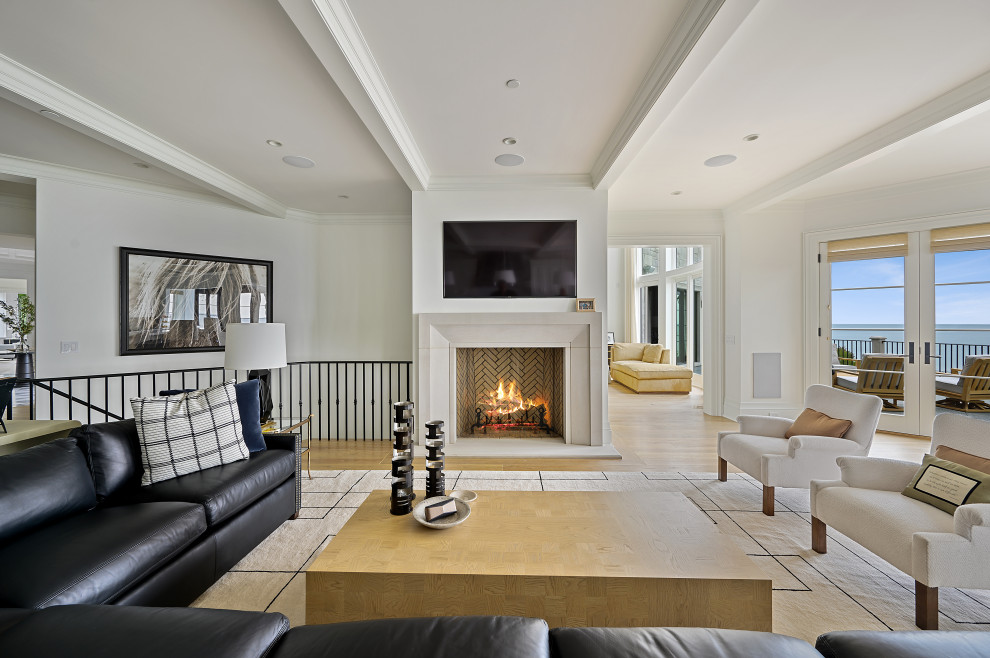 На фото: открытая гостиная комната в стиле неоклассика (современная классика) с белыми стенами, паркетным полом среднего тона, стандартным камином, телевизором на стене и коричневым полом