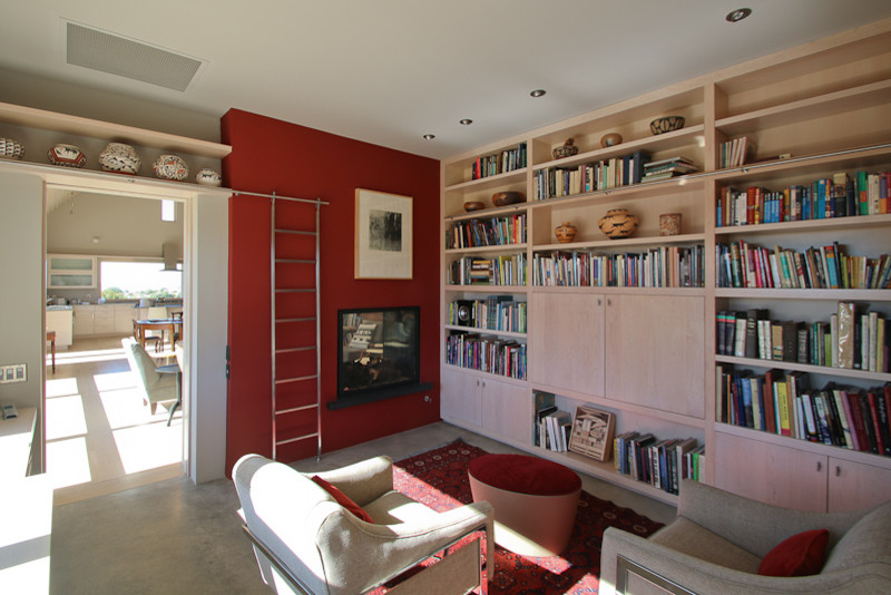 Foto de biblioteca en casa cerrada actual de tamaño medio con paredes blancas, suelo de cemento, chimenea de doble cara y televisor retractable