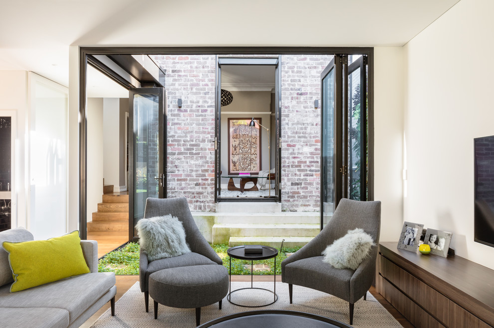 Immagine di un soggiorno design aperto con pareti bianche, pavimento in legno massello medio, TV a parete e pavimento marrone