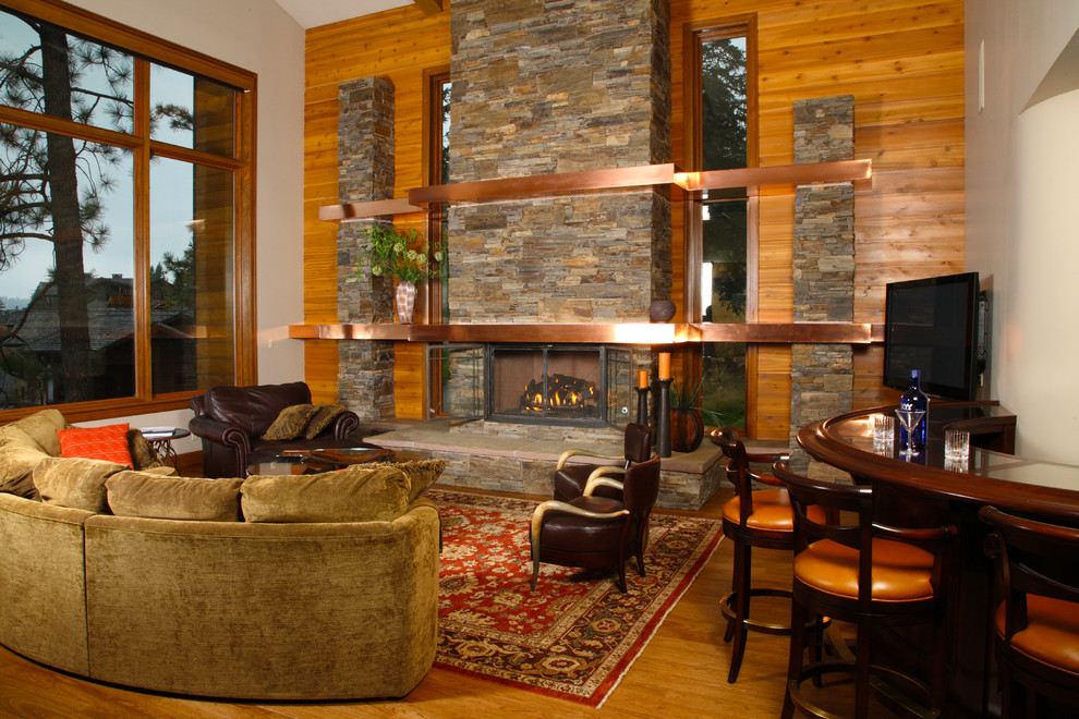 Ejemplo de salón para visitas abierto de estilo americano grande con paredes marrones, suelo de madera en tonos medios, todas las chimeneas, marco de chimenea de piedra y televisor colgado en la pared