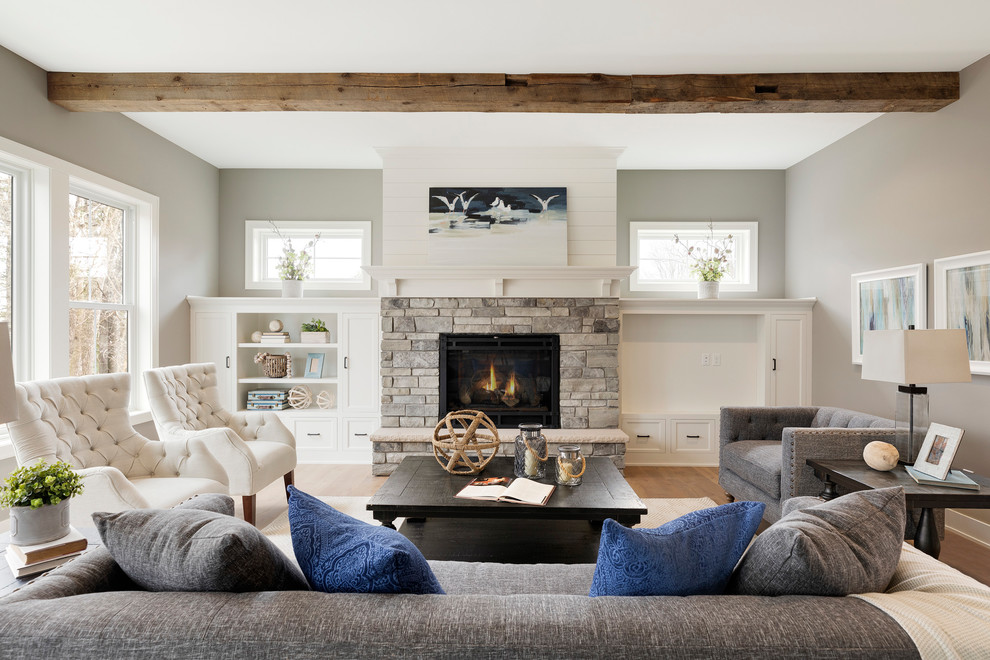 Aménagement d'un grand salon classique ouvert avec un mur gris, un sol en bois brun, une cheminée standard, un manteau de cheminée en pierre, un téléviseur encastré et un sol beige.