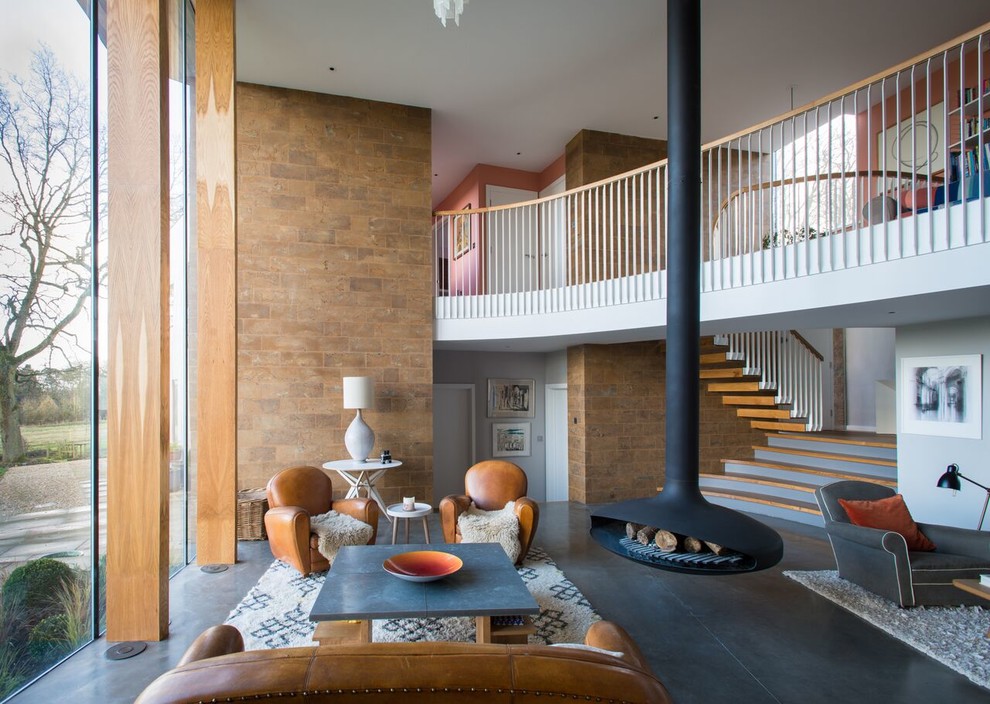 Large contemporary open plan living room in Oxfordshire with a hanging fireplace, concrete flooring and grey floors.