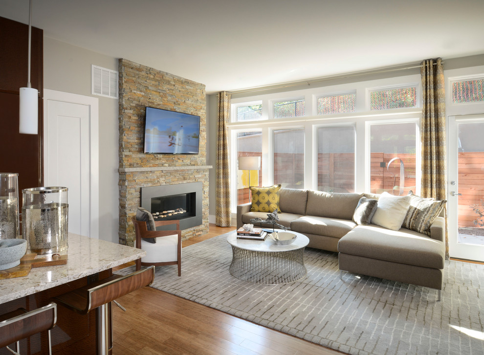 Источник вдохновения для домашнего уюта: открытая гостиная комната в современном стиле с серыми стенами, полом из бамбука, стандартным камином, фасадом камина из камня и телевизором на стене