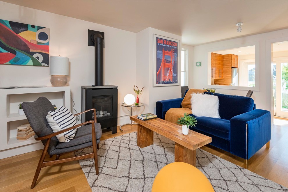 サンフランシスコにあるお手頃価格の小さなコンテンポラリースタイルのおしゃれな独立型リビング (白い壁、淡色無垢フローリング、薪ストーブ、内蔵型テレビ、茶色い床、青いソファ) の写真