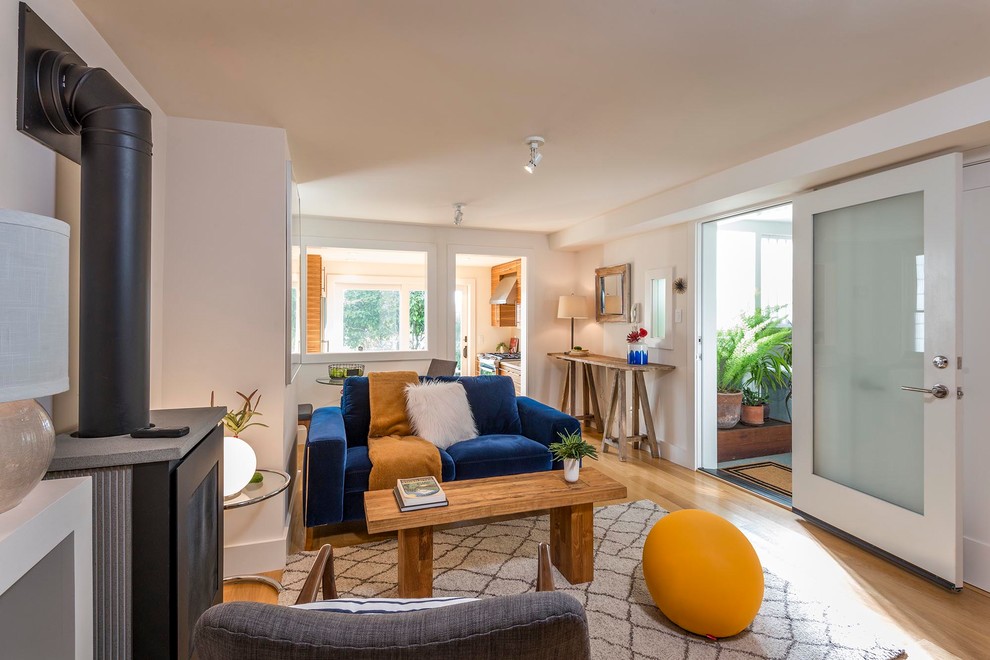 Immagine di un piccolo soggiorno minimalista chiuso con pareti bianche, parquet chiaro, stufa a legna, TV nascosta e pavimento marrone