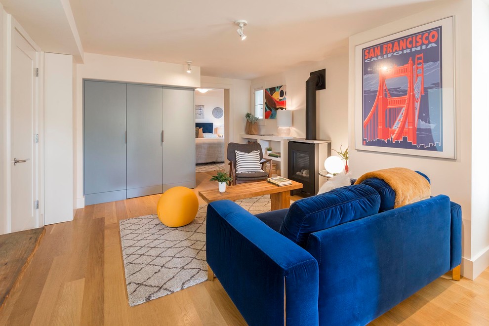 Immagine di un piccolo soggiorno moderno chiuso con pareti bianche, parquet chiaro, stufa a legna, TV nascosta e pavimento marrone