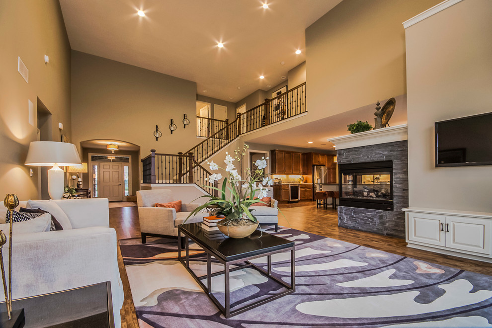 Inspiration for a large transitional open concept medium tone wood floor living room remodel in Milwaukee with beige walls, a two-sided fireplace, a stone fireplace and a wall-mounted tv