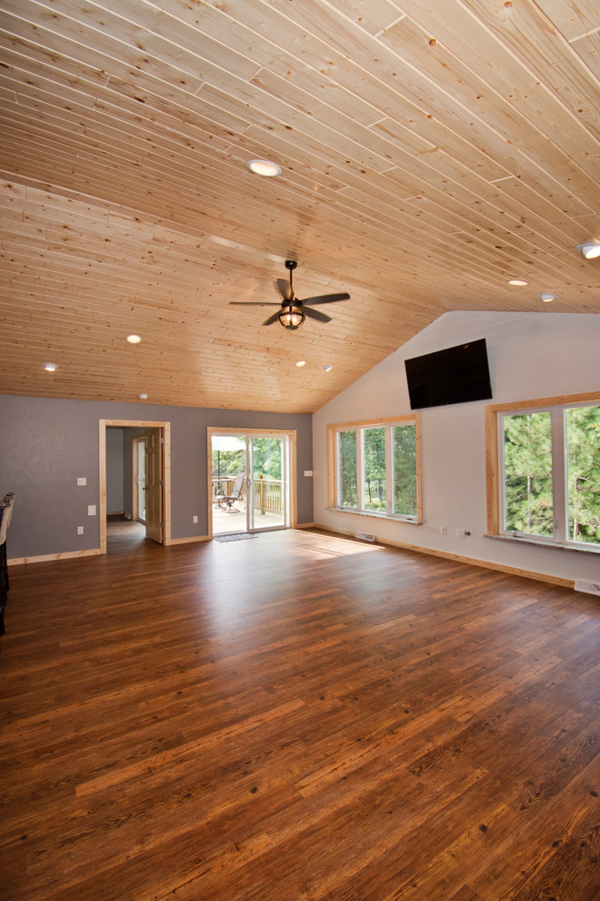 Modelo de salón abierto rústico de tamaño medio con paredes grises, suelo de madera en tonos medios, televisor colgado en la pared y suelo marrón