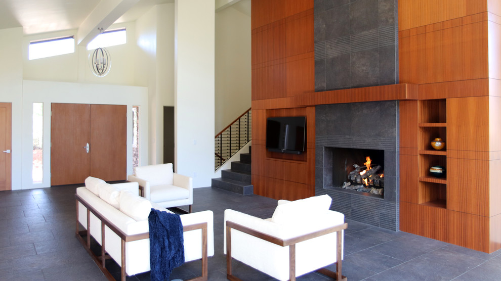 Example of a mid-sized trendy open concept ceramic tile and gray floor living room design in Phoenix with a wall-mounted tv, white walls, a standard fireplace and a tile fireplace