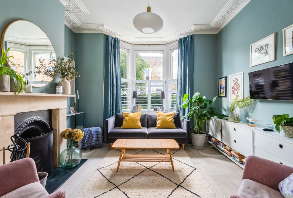 This is an example of a traditional enclosed living room in Essex with blue walls, light hardwood flooring, a standard fireplace, a wall mounted tv and beige floors.