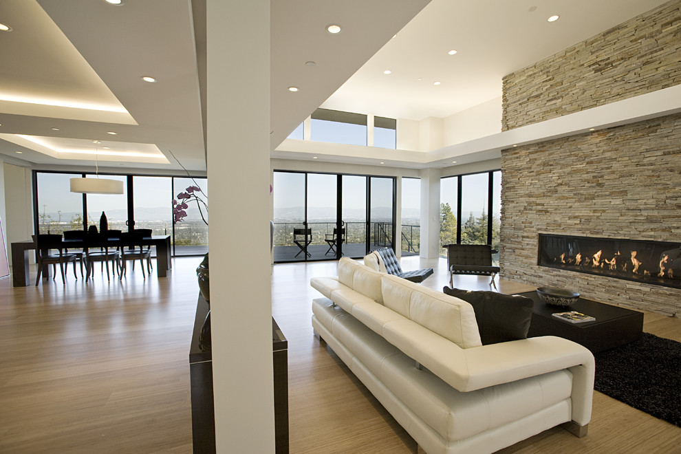 Идея дизайна: большая гостиная комната в современном стиле с светлым паркетным полом, фасадом камина из камня, белыми стенами и горизонтальным камином без телевизора