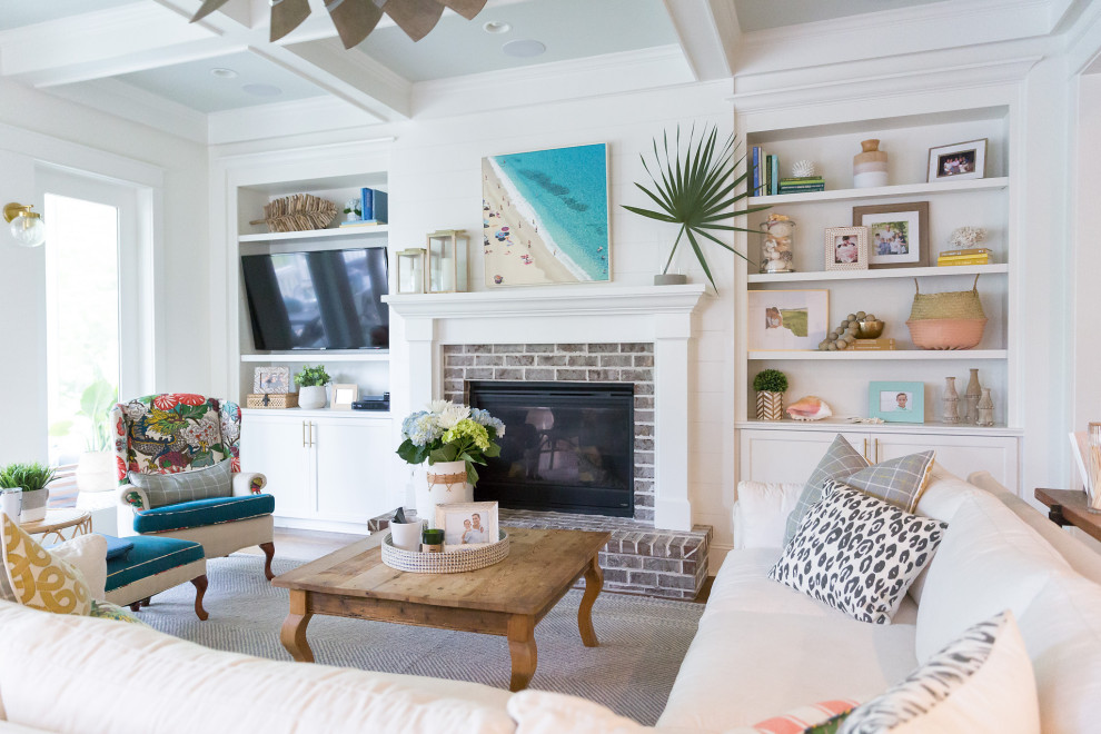This is an example of a coastal living room in Charleston with white walls, medium hardwood flooring, a standard fireplace, a brick fireplace surround and brown floors.