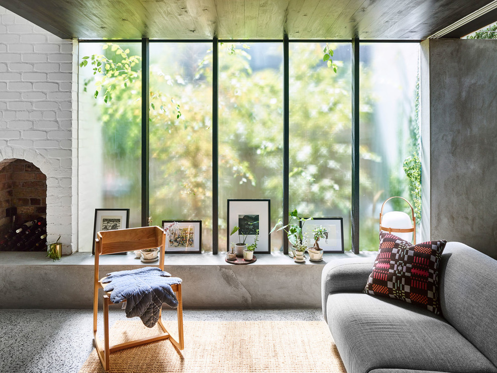 Inspiration pour un salon minimaliste de taille moyenne et ouvert avec un mur gris, sol en béton ciré, un poêle à bois, un manteau de cheminée en brique, un téléviseur dissimulé et un sol gris.