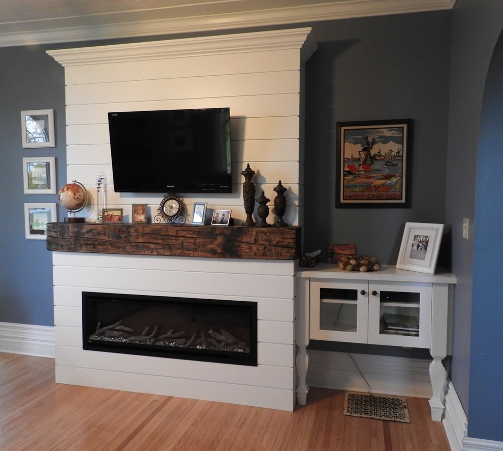 Ejemplo de salón cerrado campestre pequeño con paredes azules, suelo de madera clara, chimeneas suspendidas, marco de chimenea de madera, televisor colgado en la pared y suelo marrón