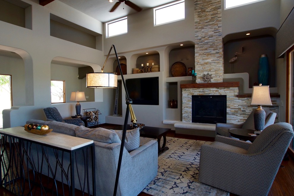 Offenes Mediterranes Wohnzimmer mit grauer Wandfarbe, braunem Holzboden, Kamin, Kaminumrandung aus Stein und TV-Wand in Phoenix