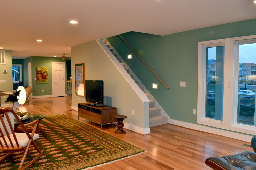 Modelo de salón abierto contemporáneo grande con paredes verdes, suelo de madera en tonos medios y televisor independiente
