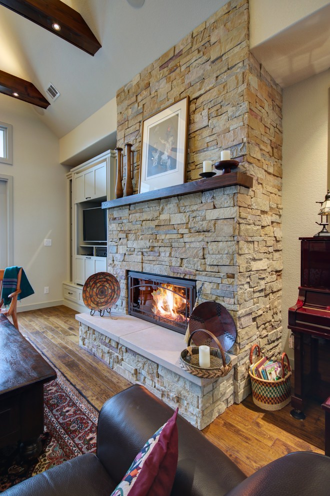 Exemple d'un salon craftsman de taille moyenne et ouvert avec un mur beige, un sol en bois brun, une cheminée standard, un manteau de cheminée en pierre et un téléviseur encastré.