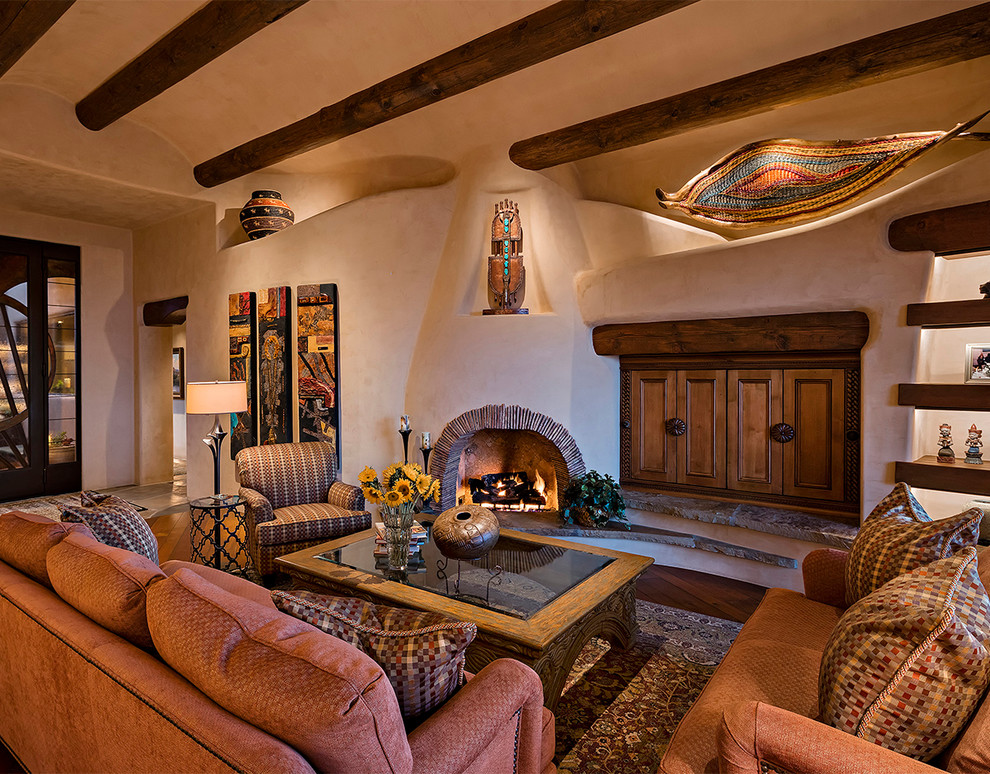 Exemple d'un salon sud-ouest américain ouvert avec un mur beige, une cheminée d'angle, un téléviseur dissimulé, un sol en bois brun et un manteau de cheminée en plâtre.