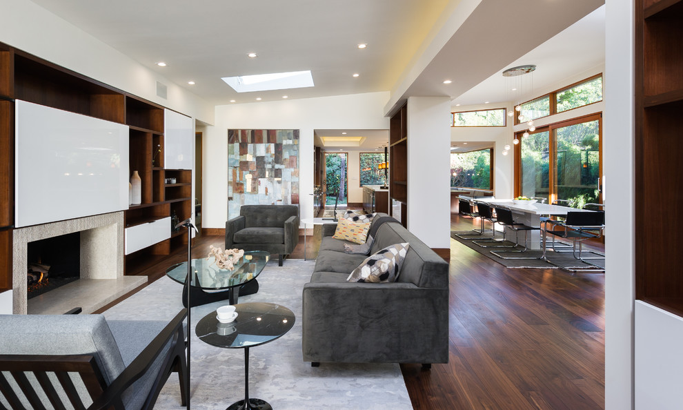 Mittelgroßes, Offenes Modernes Wohnzimmer mit weißer Wandfarbe, braunem Holzboden, Kamin, Kaminumrandung aus Stein und verstecktem TV in Los Angeles