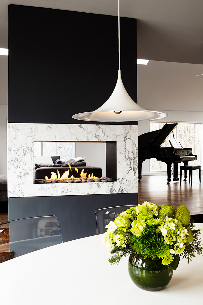 Modelo de salón abierto minimalista grande con paredes grises, suelo de madera oscura, chimenea de doble cara y marco de chimenea de piedra