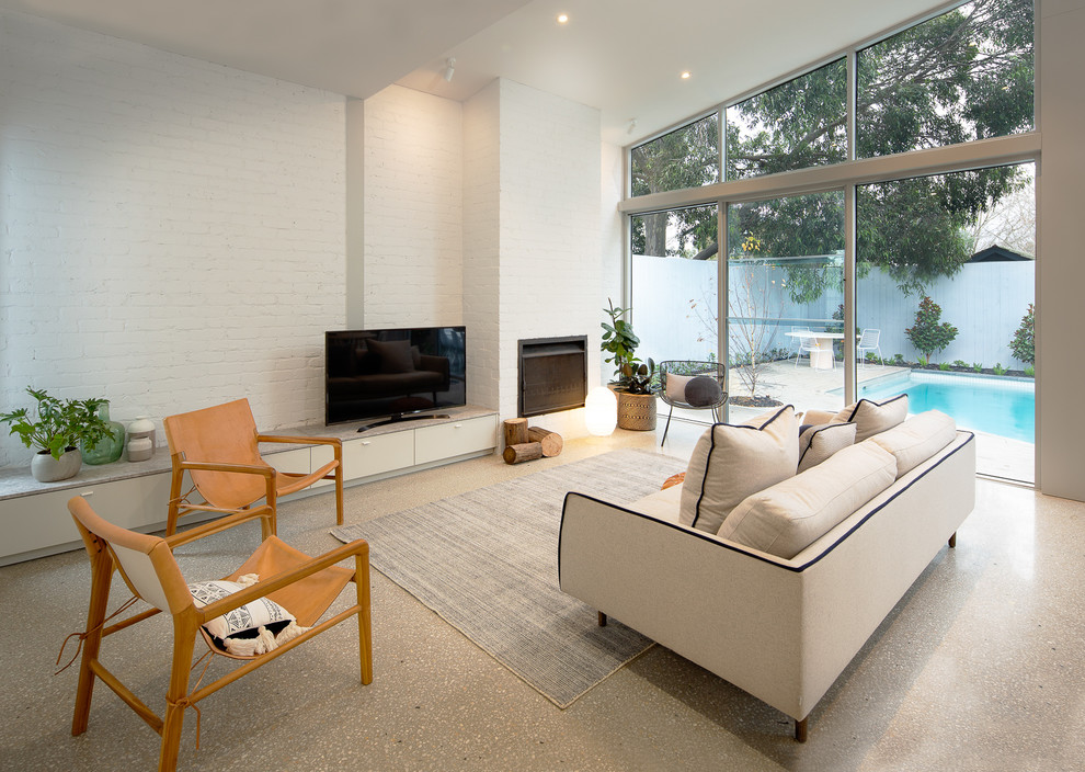 Mittelgroßes, Offenes Wohnzimmer mit weißer Wandfarbe, Betonboden, Kamin, Kaminumrandung aus Backstein, freistehendem TV und grauem Boden in Melbourne