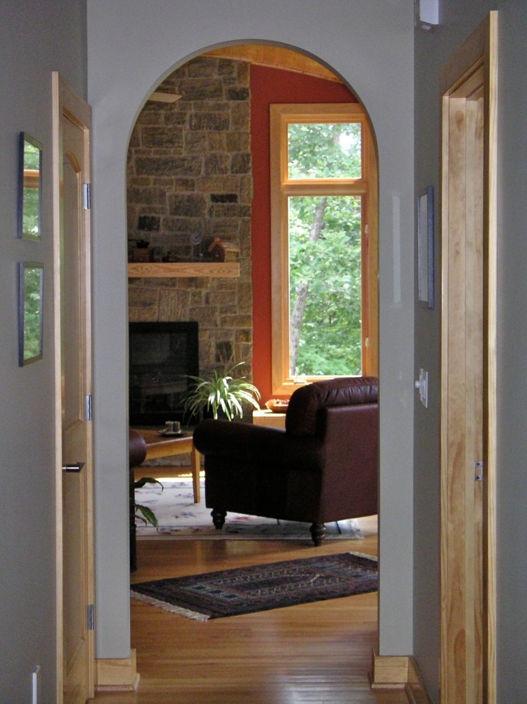 На фото: изолированная гостиная комната в стиле рустика с оранжевыми стенами, светлым паркетным полом, стандартным камином и фасадом камина из камня