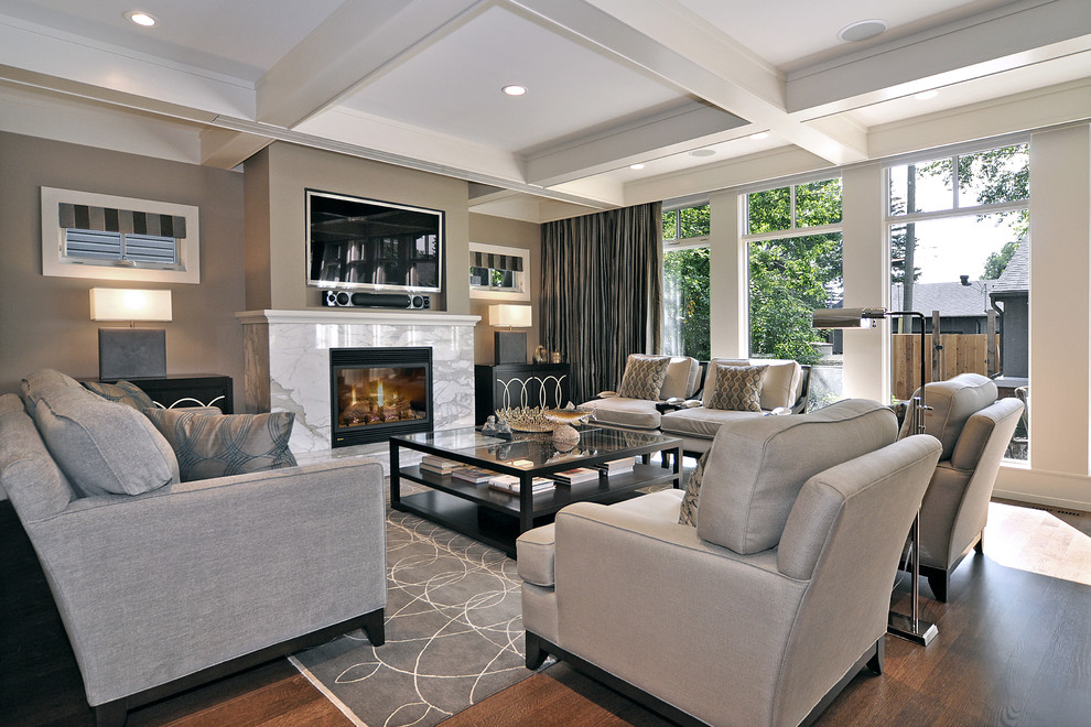 Klassisches Wohnzimmer mit Kaminumrandung aus Stein, beiger Wandfarbe, braunem Holzboden, TV-Wand und braunem Boden in Calgary