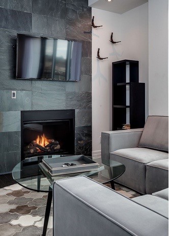 Diseño de salón actual de tamaño medio con paredes grises, suelo de madera oscura, marco de chimenea de piedra y televisor colgado en la pared