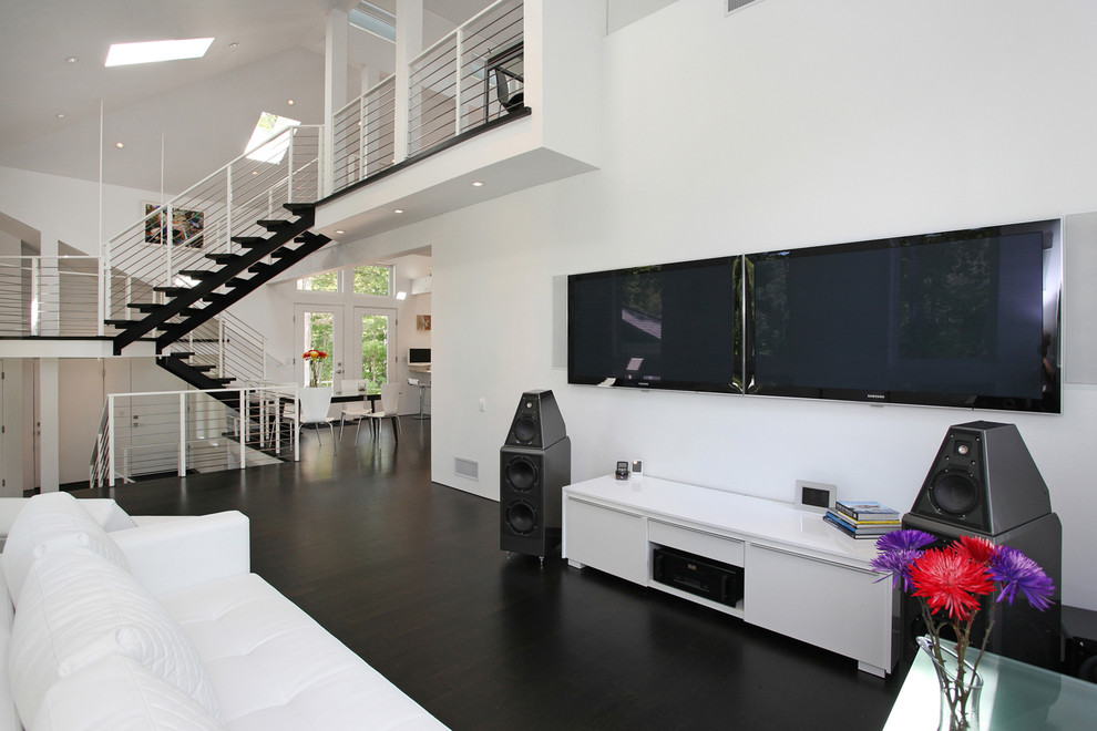 Bild på ett funkis allrum med öppen planlösning, med ett musikrum, vita väggar, mörkt trägolv och en väggmonterad TV