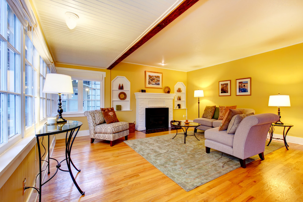 Inredning av ett klassiskt mellanstort separat vardagsrum, med ett finrum, gula väggar, ljust trägolv, en standard öppen spis och en spiselkrans i tegelsten