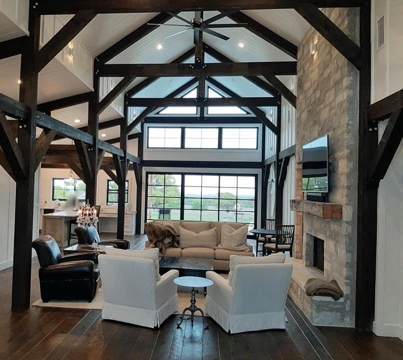 This is an example of a large farmhouse open plan living room in Austin with white walls, dark hardwood flooring, a standard fireplace, a stacked stone fireplace surround, a wall mounted tv, brown floors, exposed beams and wood walls.