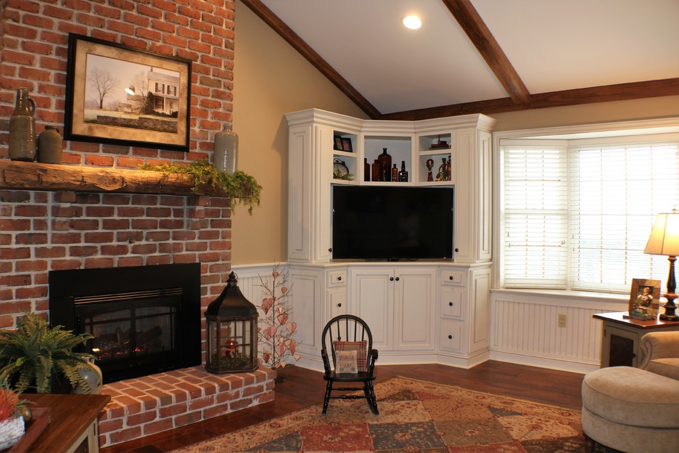 Cette image montre un grand salon traditionnel fermé avec une bibliothèque ou un coin lecture, un mur beige, un sol en bois brun, une cheminée standard, un manteau de cheminée en brique et un téléviseur encastré.