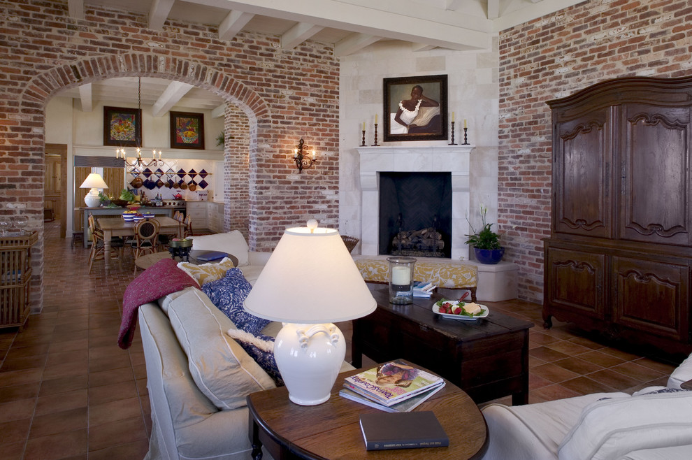 Cette image montre un grand salon ethnique ouvert avec tomettes au sol, une cheminée d'angle, un manteau de cheminée en pierre et un téléviseur dissimulé.