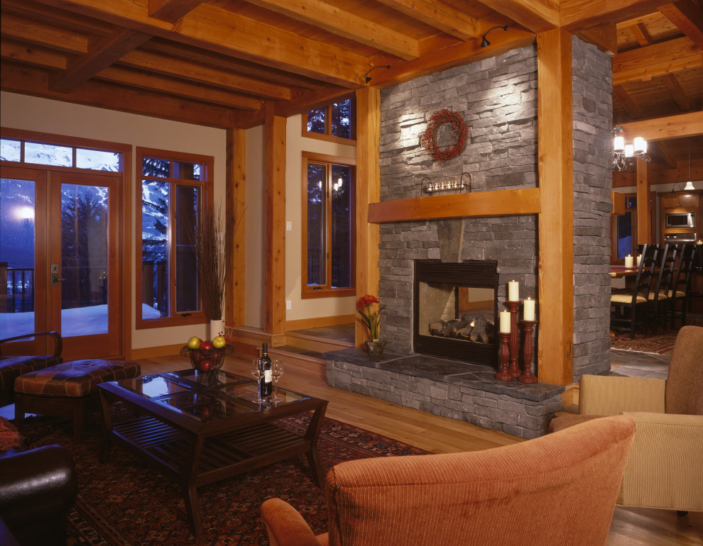 Inspiration for a mid-sized craftsman open concept medium tone wood floor, brown floor and exposed beam living room remodel in Vancouver with white walls, a two-sided fireplace and a stone fireplace