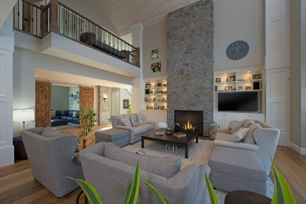 Large mountain style open concept medium tone wood floor and brown floor living room photo in Other with beige walls, a standard fireplace, a stone fireplace and a media wall