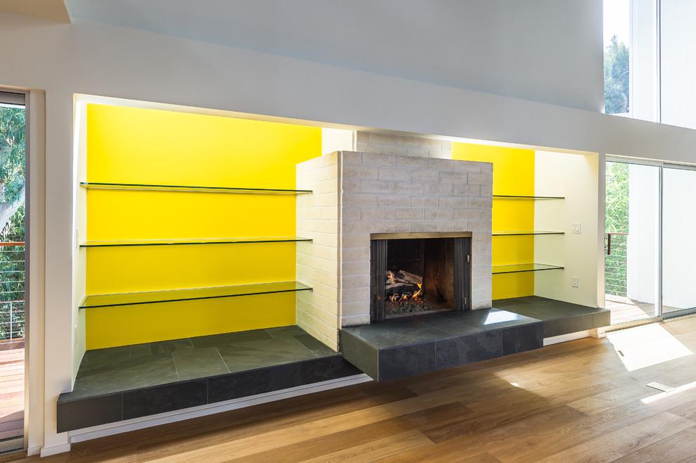 Foto på ett stort 60 tals loftrum, med ett bibliotek, gula väggar, ljust trägolv, en standard öppen spis och en spiselkrans i trä