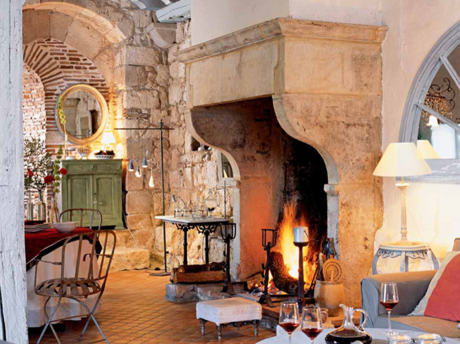 Cette image montre un grand salon méditerranéen ouvert avec un mur beige, tomettes au sol, une cheminée standard, un manteau de cheminée en pierre et aucun téléviseur.