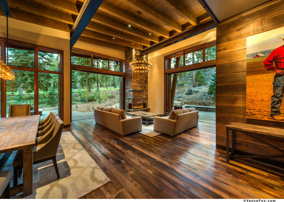 Foto de salón abierto rural extra grande con suelo de madera en tonos medios, marco de chimenea de piedra, paredes marrones y chimenea de esquina