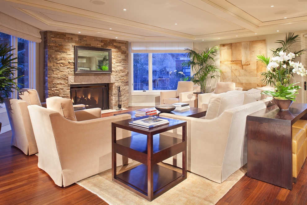 На фото: гостиная комната в современном стиле с белыми стенами, паркетным полом среднего тона, стандартным камином и фасадом камина из камня