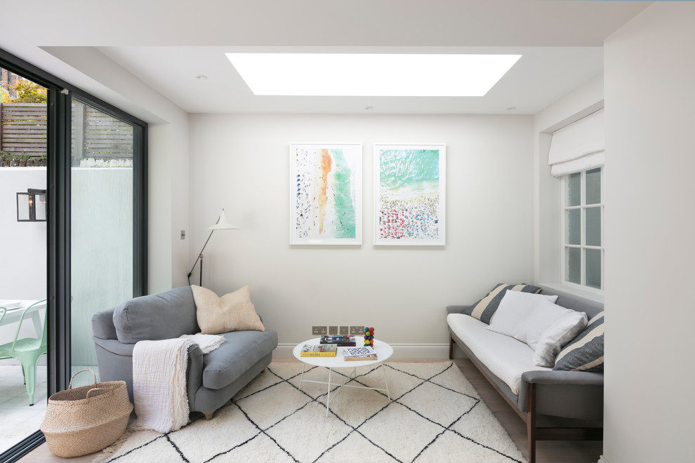 Стильный дизайн: открытая гостиная комната среднего размера в скандинавском стиле с серыми стенами, светлым паркетным полом и телевизором на стене - последний тренд